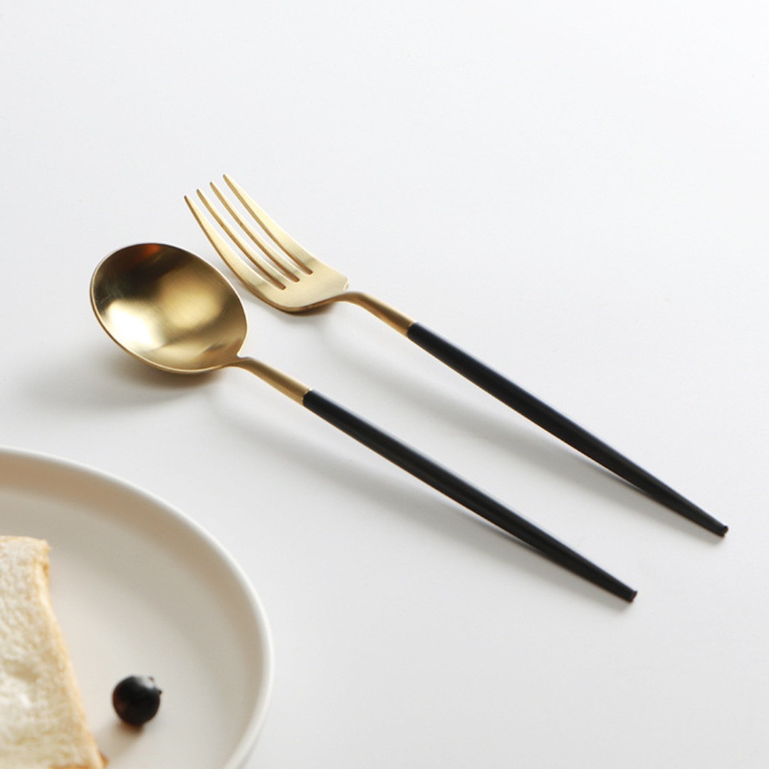 Minimalistisches Besteckset in Gold und Schwarz aus Edelstahl 18/10 auf weißem Teller
